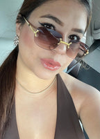 A close-up selfie of a woman wearing gold-framed  sunglasses with brown tinted lenses and a brown halter top inside a car AlfiEyewear 